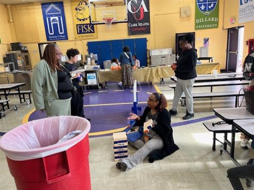 three adults and one student playing giant Jenga on the floor
